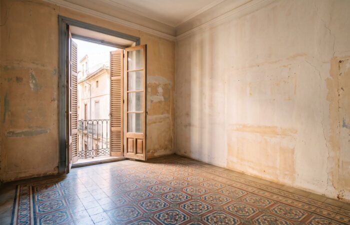 Estancia vacía de un piso antiguo de Valencia con suelo hidráulico original, techo alto con moldura y balcón de madera